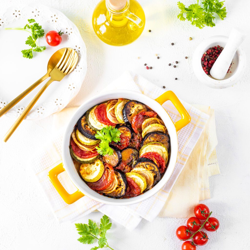 Delicious vegetable ratatouille in a white baking dish on a wooden background